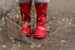 Child wearing red rain boots jumping into a puddle